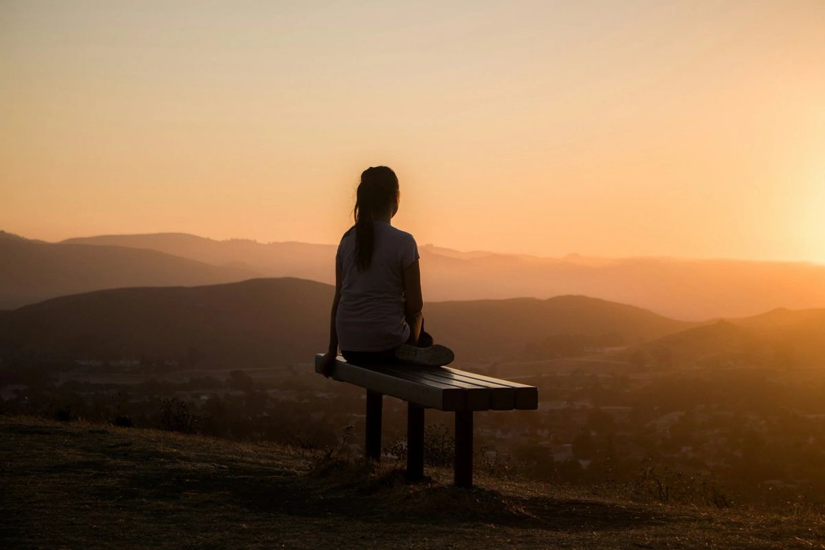A woman sitting on a bench watching the sunset over the hills